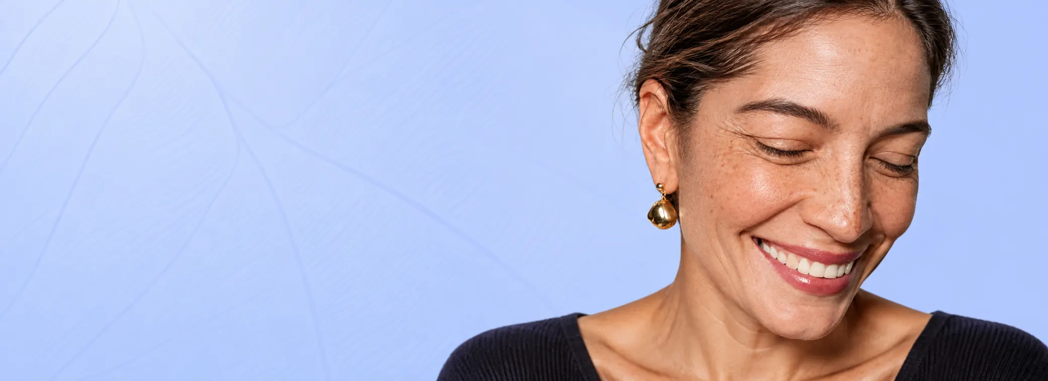 Mulher sorrindo, de olhos baixos, com brinco dourado